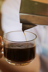 A man pouring fresh hot coffee from geyser coffee maker into glass cup.