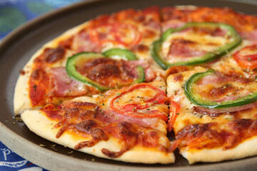 Italian pizza with ham, mozzarella cheese, tomato and bell pepper on ceramic plate.
