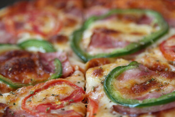 Italian pizza with ham, mozzarella cheese, tomato and bell pepper on ceramic plate.