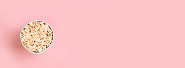 Paper bowl with salted popcorn on pink background. Top view with copy space. Flat lay