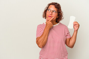 Middle age woman holding a compress isolated on white background looking sideways with doubtful and skeptical expression.