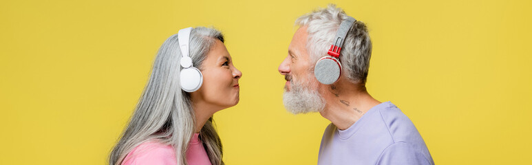side view of funny multiethnic and middle aged couple in wireless headphones looking at each other...