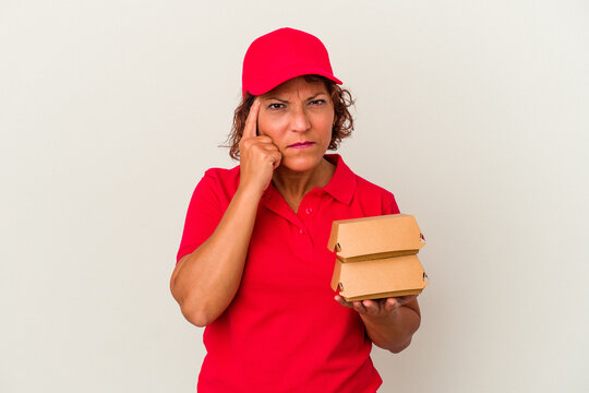 Middle age delivery woman taking burguers isolated on white background pointing temple with finger, thinking, focused on a task.