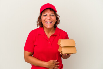 Middle age delivery woman taking burguers isolated on white background laughing and having fun.