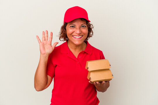 Middle age delivery woman taking burguers isolated on white background smiling cheerful showing number five with fingers.