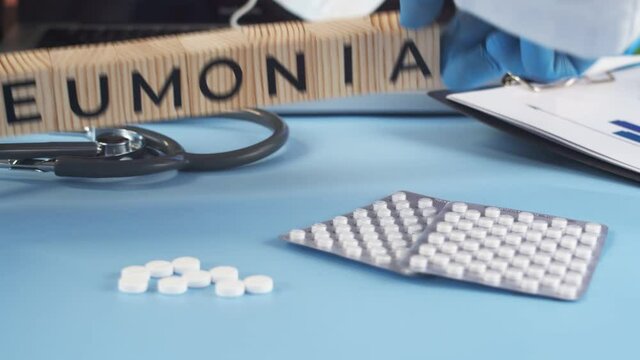 Wooden cubes with inscription pneumonia are placed by doctor on table. Appearing cubes with the word pneumonia complement the medical table full of medicines