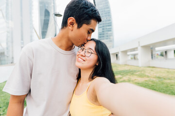 Young asian couple in love outdoors taking selfie kissing forehead smiling happy