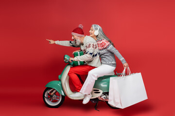 cheerful middle aged asian woman holding shopping bags while riding moped with husband pointing...