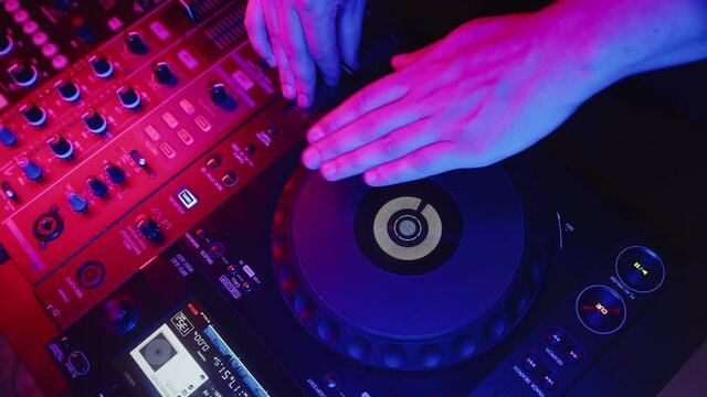 DJ works behind DJ setup and adjusts fader. Male hand rotates platform on digital mixing console, closeup, top view. Concept of modern music in nightclub