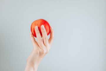 Red apple in female hand isolated on grey wall background. Apple vitamin snack. Healthy nutrition diet.