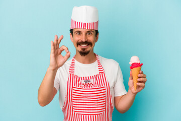 Young caucasian ice cream maker holding a ice cream isolated on blue background cheerful and confident showing ok gesture.