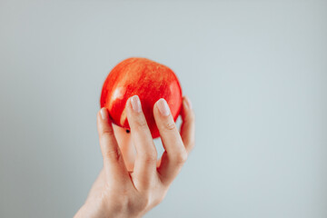 Female hand is holding healthy red apple on a grey background. Healthy nutrition diet. Minimal fruit concept.