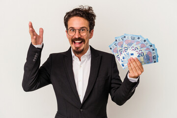 Young caucasian man holding banknotes isolated on white background receiving a pleasant surprise,...