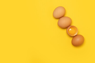 Raw brown chicken eggs and one broken egg with yolk on yellow background