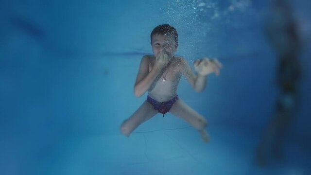 Pool fun. Preteen boy swims underwater in the pool and looks into the camera. Boy tries to hold his breath underwater