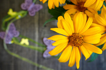 close yellow heliopsis flowers in a vase on a wooden table with wooden lilac butterflies . top view