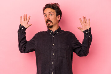 Young caucasian man isolated on pink background being shocked due to an imminent danger