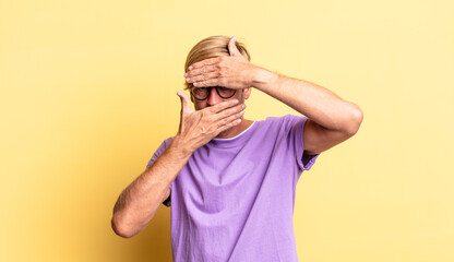handsome blond adult man covering face with both hands saying no to the camera! refusing pictures...