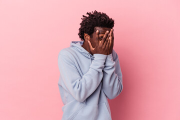 Young african american man isolated on pink background blink through fingers frightened and nervous.