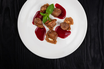 Delicacy Fried pork meat with zucchini puree and berries sauce decorated with mint on white plate on black wooden background