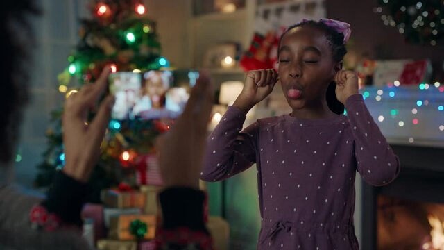 christmas funny african american girl making faces for mother taking photos using smartphone having fun enjoying festive holiday memories at home 4k 