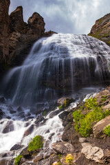 Majestic waterfall in the mountains, a mountain river falls from a high cliff onto stones on a sunny day, long exposure