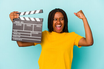 Young african american woman holding a clapperboard isolated on blue background  raising fist after...