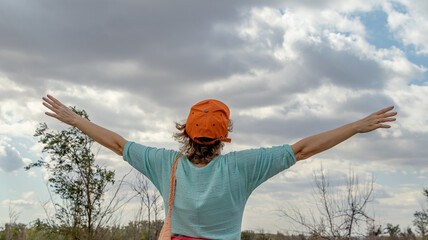 The girl spreads her arms wide and admires the sky. A picture from the back. Soft focus