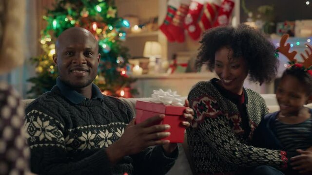 Young African American Man Opening Christmas Presents Unwrapping Gift Enjoying New Socks Celebrating Festive Holiday With Family And Friends At Home 4k