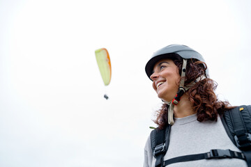 Side view of cheerful woman with helmet and paragliding equipment outdoors. Panoramic view of...