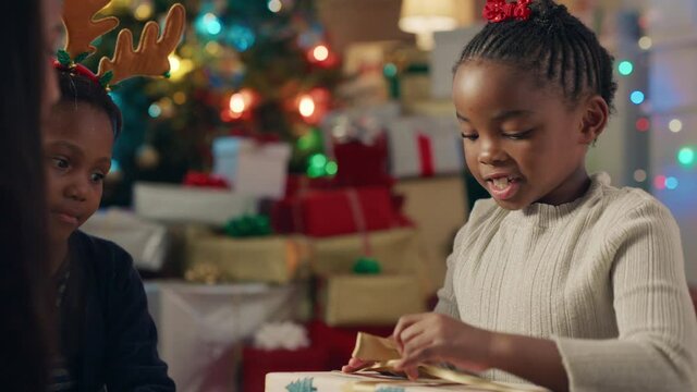 happy african american girl unwrapping christmas presents excited for special gift children having fun enjoying festive holiday celebration with family and friends 4k