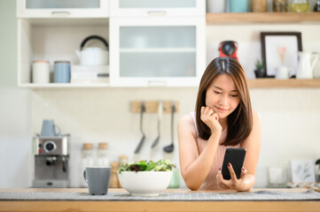 Obraz na płótnie Canvas Smiling beautiful asian woman using smartphone mobile in the kitchen