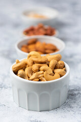 Types of assorted nuts in white ceramic bowls. Almond, cashew, peanut ground. Food vertical high key photo. Vegan vitamin products