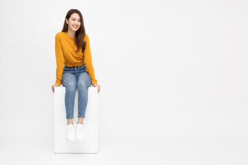 Portrait of young Asian woman sitting on white box isolated over white background, Full body...