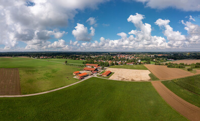 Aerial view over a ranch with horses and a village in the background under a blue, wonderful fluffy...