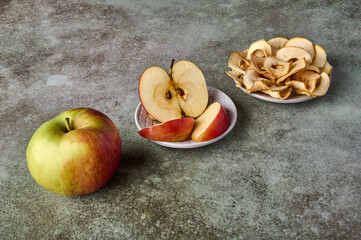 Apples chips, slices and apple fruit on rustic wooden background. Perspective view, selective focus
