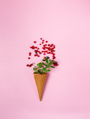Waffle ice cream cone with frozen cranberries and green twigs. Top view on a pink background.