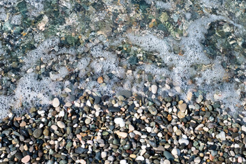 pebbly sea beach, the pebbles are half covered with a sea wave