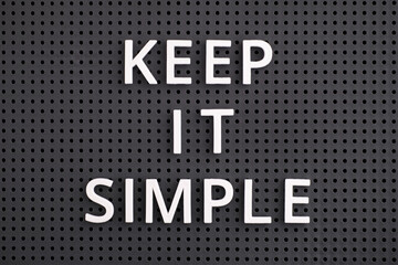 Phrase Keep It Simple spelled out with white letters on a gray pegboard. Close-up.