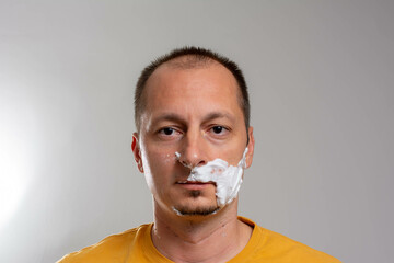 Mature handsome man shaving in front of mirror. Man with looking at camera and covering face with...