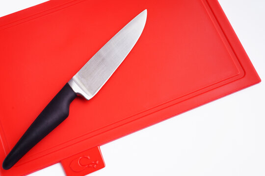 Bright Red Clean Plastic Cutting Board With A Kitchen Knife On A White Background.