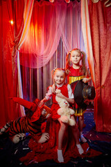 Small girls during a stylized theatrical circus photo shoot in a beautiful red location. Young models posing on stage with curtain. Twin sisters or female friends together