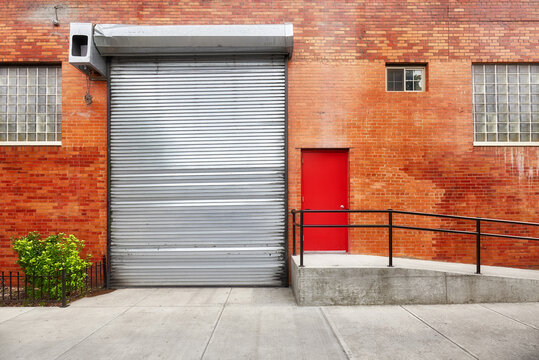 Empty street with brick wall building with automatic rolling shutter, New York, USA.