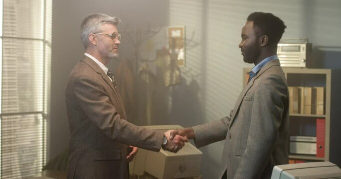 Strong agreement. Waist up of handshake with gratitude. Two diverse men shaking hands in acknowledgement of partnership. Retro office concept - Powered by Adobe