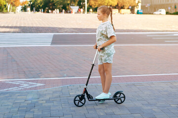 Cute teen girl rides around town on a scooter sunny summer day.