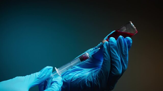 Doctor filling syringe with red solution. Nurse wearing protective gloves showing sample of medicine, vaccination against covid-19, laboratory research concept. Coronavirus vaccine.