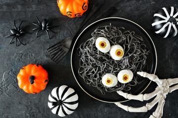 Halloween eyeball spaghetti. Top view table scene over a dark background with orange, black and...