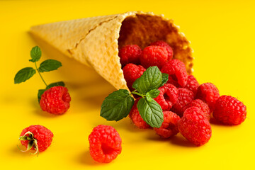 Raspberry explosion in ice cream waffle cone on yellow table. View from above. Healthy food concept. Minimalism.