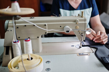 Female hands stitching fabric on professional manufacturing machine at workplace. Sewing process.