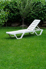 white lounge sunbed standing on green grass in the garden on a summer day. High quality photo